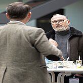 Ein Mann trägt eine braune Jacke und blickt nachdenklich zur Seite.