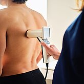 Nahaufnahme einer Untersuchung am Oberkörper einer Person, Fachkraft hält ein medizinisches Gerät.