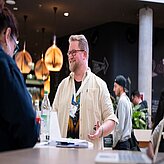 Ein Mann steht vor einem Stehtisch und lacht