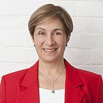 Auf dem Bild ist eine Frau mit hellen, kurzen Haaren zu sehen. Sie trägt ein weißes TShirt und ein rotes Jacket und lächelt freundlich in die Kamera.