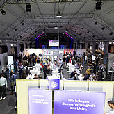 Das Bild zeigt eine große Halle mit mehreren Ausstellungsständen und vielen Menschen