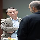 Mann in einem Jackett, der in die Kamera schaut, mit einem neutralen Hintergrund.