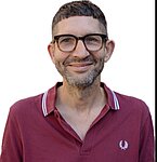 Oberkörper eines Mannes in einem dunkelroten Poloshirt mit weißem Logo auf der Brust vor weißem Hintergrund.