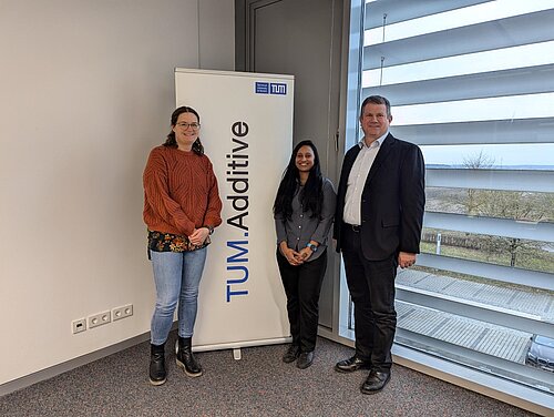 Die neue Science Managerin von TUM.Additive, Sreeja Gadhiraju, steht gemeinsam mit ihren Kollegen Prof. Katrin Wudy und Prof. Peter Mayr vor einer TUM.Additive-Leinwand