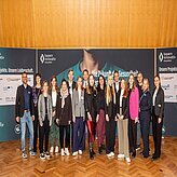 Eine Gruppe von Personen steht vor einem Hintergrund mit Text und Logos.