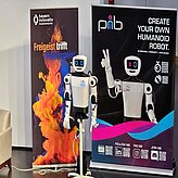 Vor zwei Roll-ups ist ein pib (printable intelligent bot und ist ein 3D-druckbarer humanoider Roboter), zu sehen.