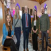 Eine Gruppe von Menschen steht in einem imposanten Raum und posiert für ein Foto