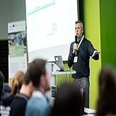 Ein Mann hält einen Vortrag, eine große Leinwand ist zu sehen