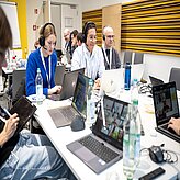 Eine Gruppe von Menschen sitzt an einem Tisch und arbeitet mit Laptops.