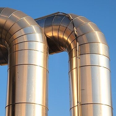 Das Bild zeigt zwei große, gebogene Metallrohre vor blauem Himmel.