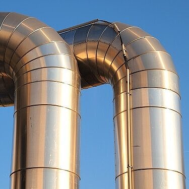 Das Bild zeigt zwei große, gebogene Metallrohre vor blauem Himmel.