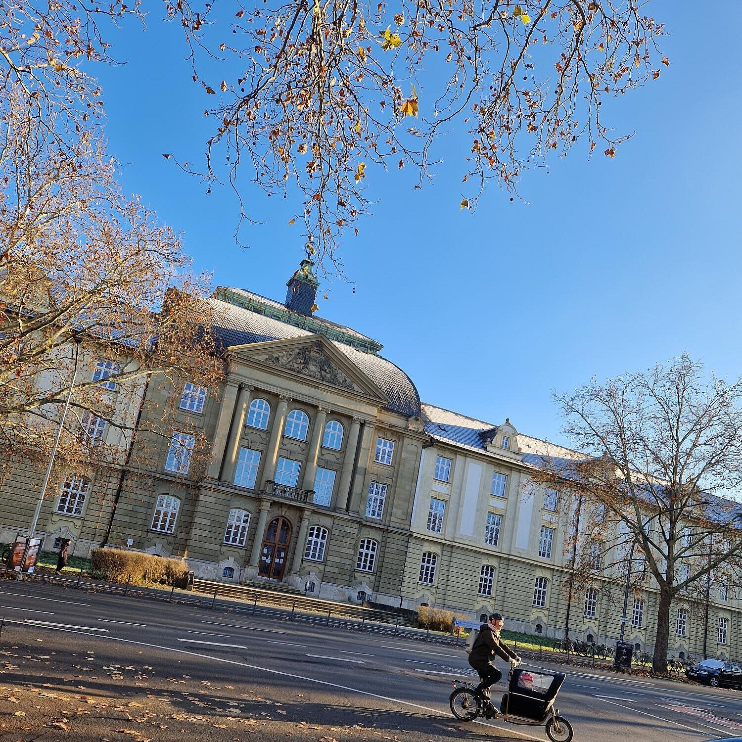 Blick auf die humanistische Fakultät in Würburg. Sonnige, herbstliche Stimmung. Ein Lastenfahrrad fährt in die rechte Richtung.,