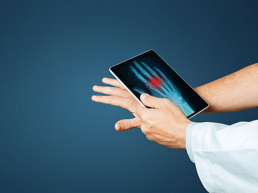Hand mit ausgestreckten Fingern, darüber ein Tablet mit Röntgenbild der Hand und rotem Markierungsbereich