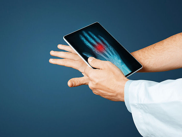 Hand mit ausgestreckten Fingern, darüber ein Tablet mit Röntgenbild der Hand und rotem Markierungsbereich