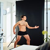  Person in Unterwäsche posiert vor schwarzem Hintergrund in einem Fotostudio-Setup.