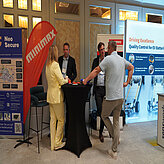 Vier Personen im Gespräch an einem Messestand beim Batteriekongress 2025, umgeben von Infobannern zu Batteriesicherheit und Qualitätssicherung.