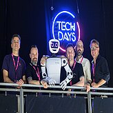Mathis Nitschke, Director, Sofilab, TJ Graebe, Projektmanager Humanoide Robotik, isento GmbH, Dr. Jürgen Baier, CEO, isento GmbH, Andreas Auberger, Leitung CreativeTechHUB, Bay-ern Innovativ GmbH und Prof. Daniel Nusser, Studiengangsleitung Prozess- und Produktdesign, DIPLOMA Hochschule stehen gemeinsam mit einem humanoiden Roboter vor einem beleuch-teten „TECH DAYS“-Logo und blicken in die Kamera.