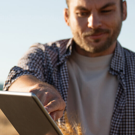 Eine Frau und ein Mann stehen auf einem Feld. Der Mann zeigt der Frau etwas auf einem Tablet.