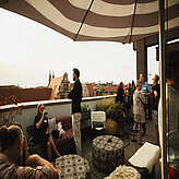 Mehrere Gäste stehen oder sitzen auf einer Dachterrasse und unterhalten sich. Im Hintergrund ist die Nürnberger Altstadt zu sehen.