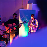 Das Bild zeigt zwei Männer, sie spielen Instrumente und einer singt