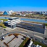 Luftaufnahme eines modernen Büro- und Industriegebäudes mit Solarpaneelen auf dem Dach an einem Kanal in einem Gewerbegebiet