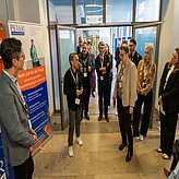 Gruppe von Menschen steht in einem Flur vor einem Informationsbanner mit Text zu Pflege und Gesundheitsversorgung