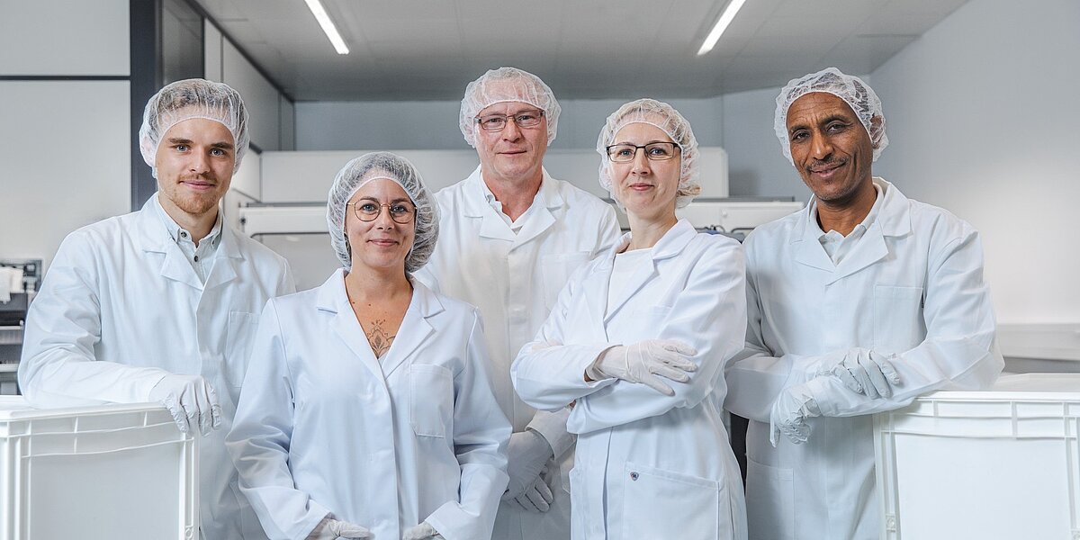 Fünf Personen in weißen Laborkitteln und Handschuhen stehen in einem Laborumfeld