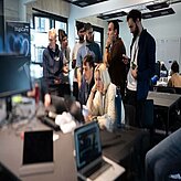 Das Bild zeigt junge Erwachsene, die konzentriert und kollaborativ an Computern arbeiten. Im Hintergrund ist das Logo "DigiCare" zu sehen.