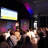 Das Bild zeigt mehrere Menschen wie sie einem Vortrag folgen