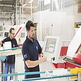 Mitarbeiter von Rupp + Hubrach Optik GmbH schaut in der Produktionsabteilung auf den Monitor einer Maschine.