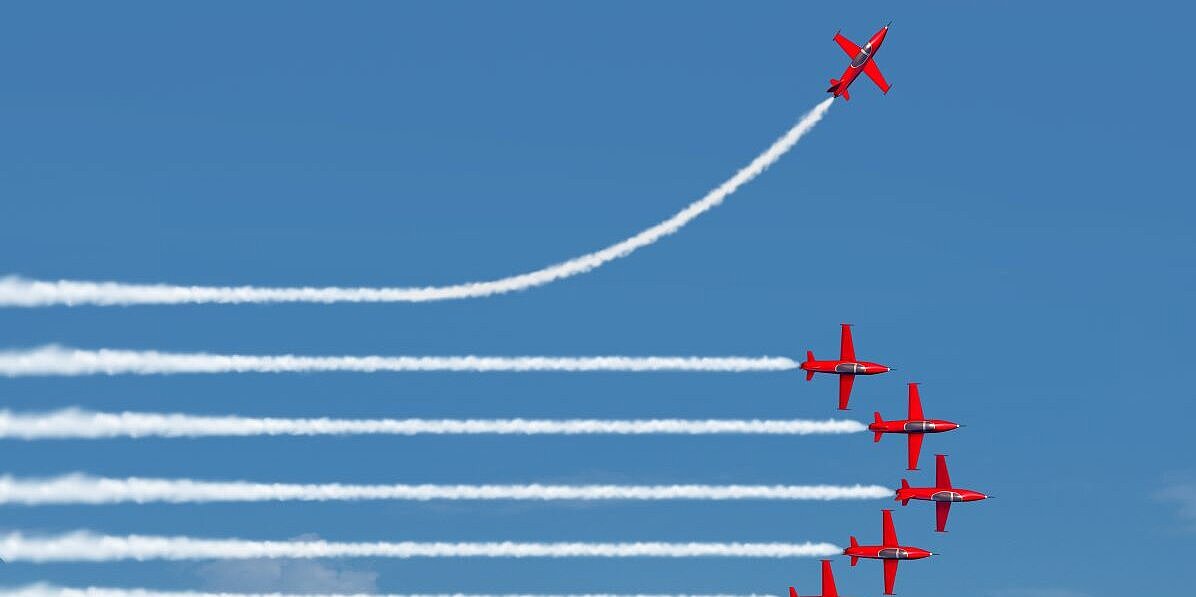 sieben rote Kunstflieger am Himmer, davon einer, der in eine andere Richtung fliegt