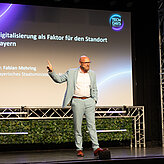 Das Bild zeigt einen Mann auf einer Bühne, er hält einen Vortrag