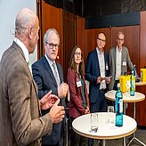 Fünf Personen stehen um Stehtische herum und unterhalten sich 