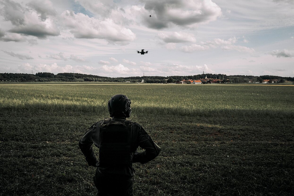 Person in Militär-Schutzkleidung sieht eine Drohne an, die im Himmel fliegt