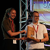 Das Bild zeigt eine junge Frau welche einem jungen Mann einen Preis überreicht