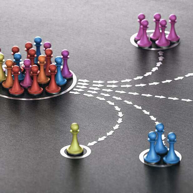 Farbige Spielfiguren, die aus einer großen Gruppe heraus in kleinere, farblich sortierte Gruppen aufgeteilt werden, verbunden durch gepunktete Pfeile auf dunklem Untergrund.