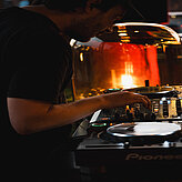 Ein DJ steht hinter einem Mischpult und bedient die Musiktechnik.