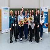 Gruppe von Menschen steht vor zwei aufrechten Bannern mit Texten zu Pflegeinnovationen und PPZ Nürnberg, drei Personen halten Blumensträuße