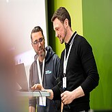 Zwei Männer stehen vor einem grünen Hintergrund