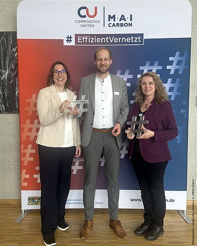 Drei Teilnehmende vor einem Banner mit Hashtag Figuren in der Hand