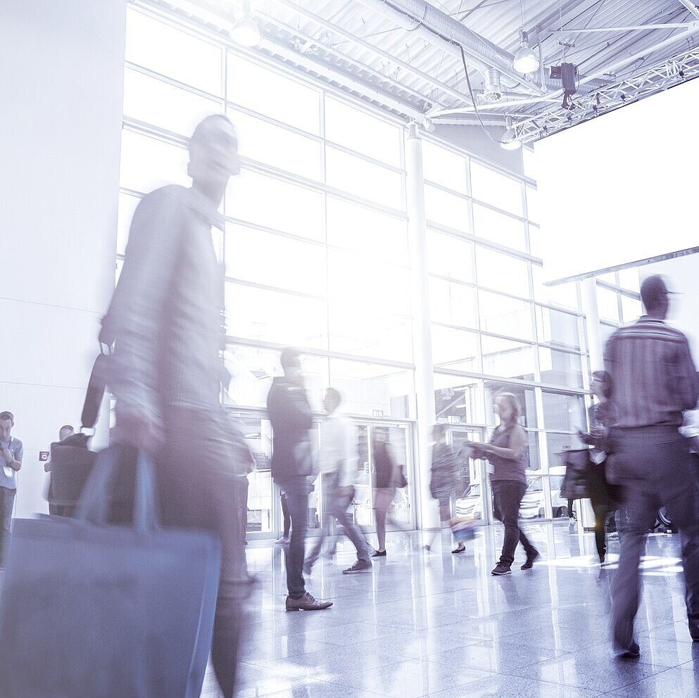 Mehrere Besucher laufen durch eine Messehalle
