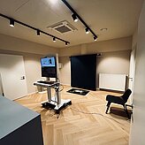 Raum mit medizinischem Gerät, schwarzem Hintergrund und Holzfußboden, Kabel am Boden sichtbar.