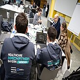 Menschen sitzen an einem Tisch und arbeiten. Sie tragen beiden den gleichen Hoodie