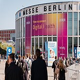 Menschenmenge vor dem runden Eingangsgebäude der Messe Berlin mit großen Bannern zur DMEA Digital Health