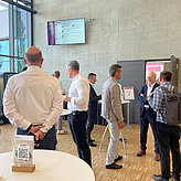 eilnehmende der Veranstaltung Textil Innovativ – Textilindustrie im zirkulären Wandel im Gespräch im Foyer während einer Networking-Pause.