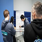 Eine Gruppe von Menschen steht um ein Whiteboard und diskutiert gemeinsam Ideen.
