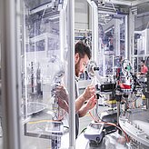 Mann arbeitet an komplexer Maschine mit vielen Kabeln und Metallteilen in einem Labor oder einer Werkstatt