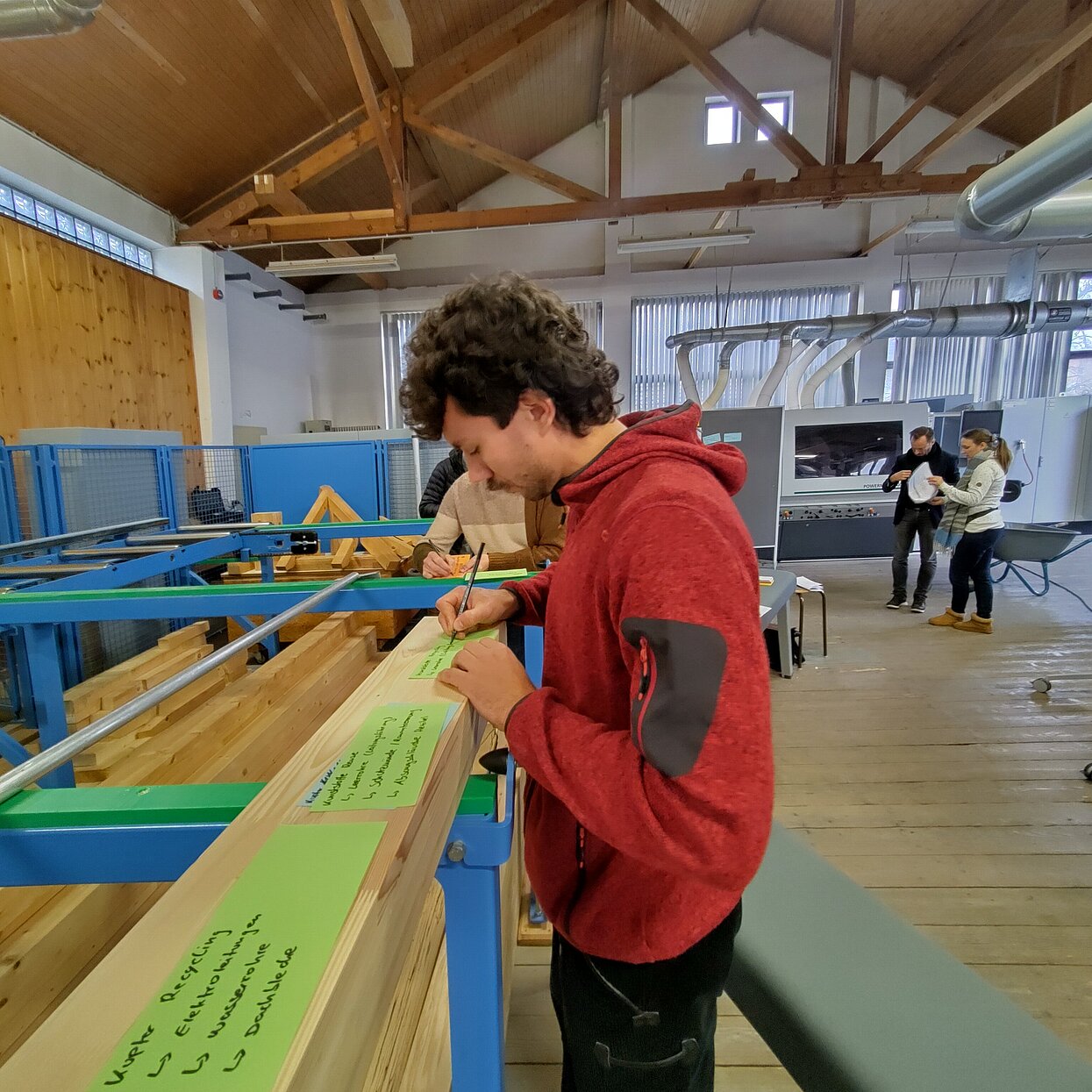 Ein Student erarbeitet etwas auf grünen Moderationskarten in einem Labor-Sägewerk. 