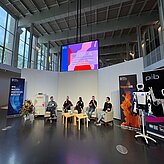 Panel: Mathis Nitschke, Komponist, Technologe und Unternehmer bei der Sofilab GmbH in München, TJ Gräbe, Problemlöser bei der isento GmbH, Prof. Daniel Nusser, Professor und Studiengangsleitung für Prozess- und Produktdesign an der DIPLOMA Hochschule, sowie Dr. Jürgen Baier, Geschäftsführer der isento GmbH, sitzen vorne in Sesseln nebeneinander und diskutieren vor Publikum. Moderiert wird die Runde von Johanna Lison, Projektmanagerin CreativeTechHUB, Bayern Innovativ GmbH. Daneben steht der pib, (printable intelligent bot und ist ein 3D-druckbarer humanoider Roboter).
