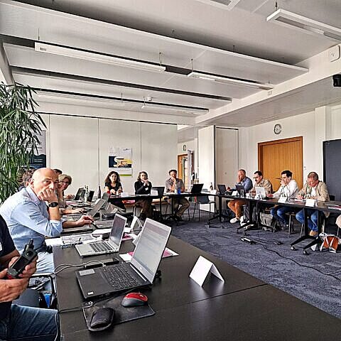 Blick in den Vortragsraum mit ca. 20 Personen an einem U-förmigen Tisch.,